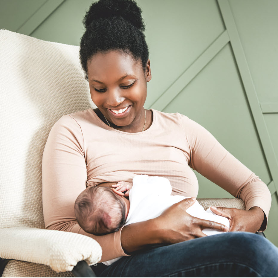 Mother looking down at the baby she holds, smiling, as she breastfeeds.